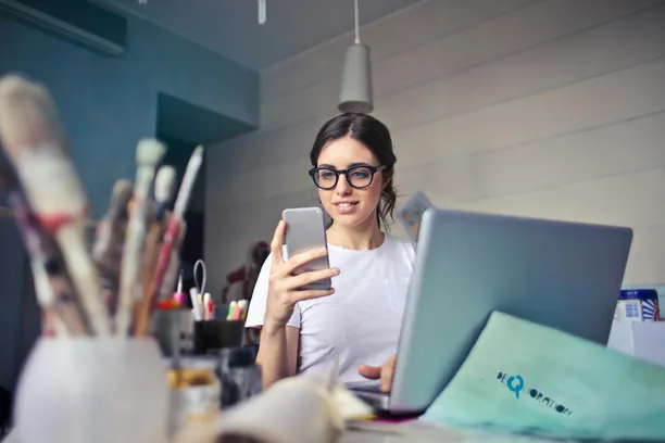 woman holding a phone smiling in front of a laptop